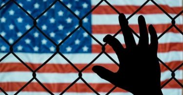 Hand on fence with American flag in background