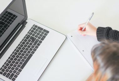 Person-taking-notes-while-looking-at-laptop-screen